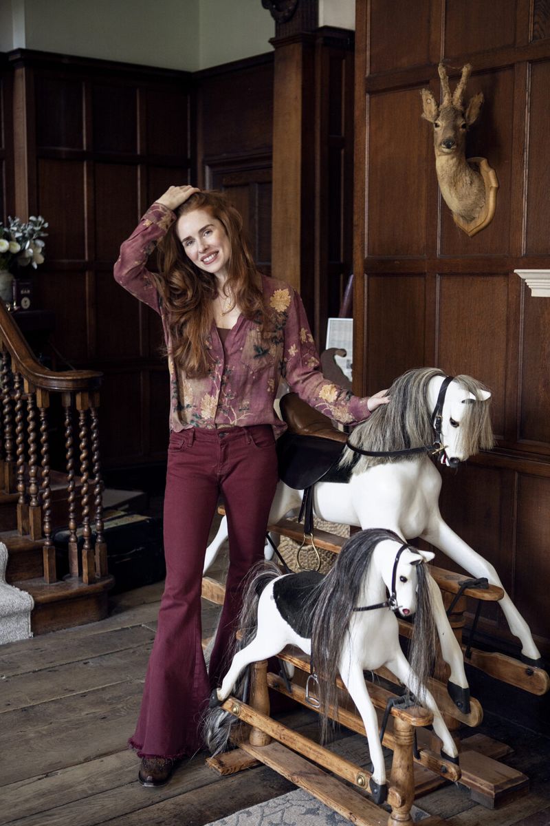 Rose beside two rocking horses in a wood-panelled hall