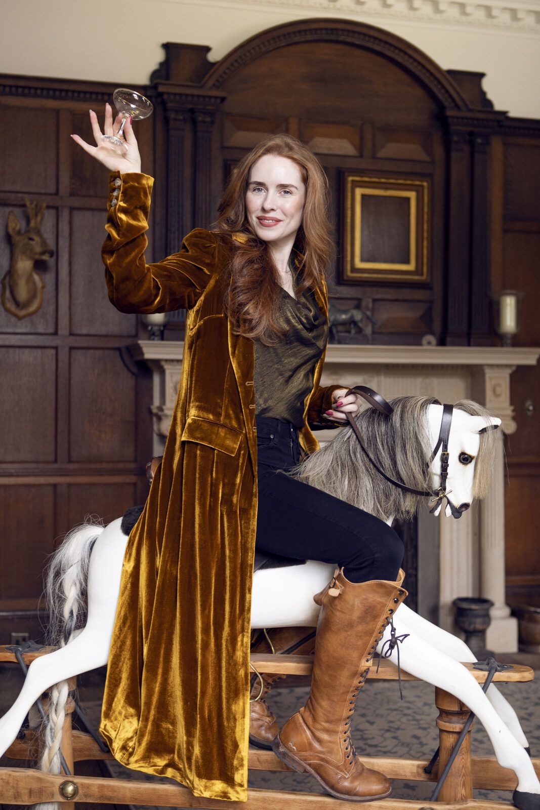 Rose Honey Morgan in a gold velvet coat, riding a rocking horse